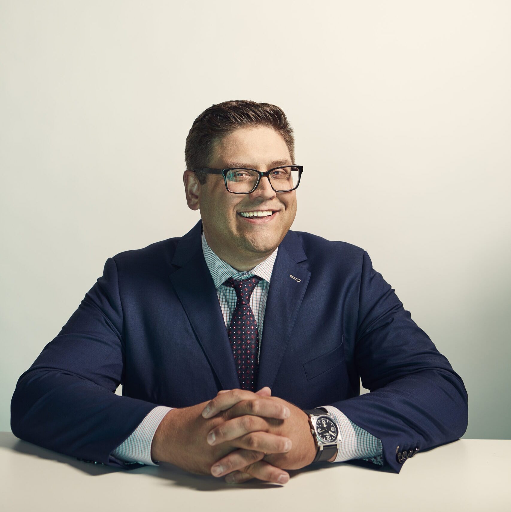 Headshot of Tim Coldwell wearing a navy suit and sitting with his hands clasped on a table.