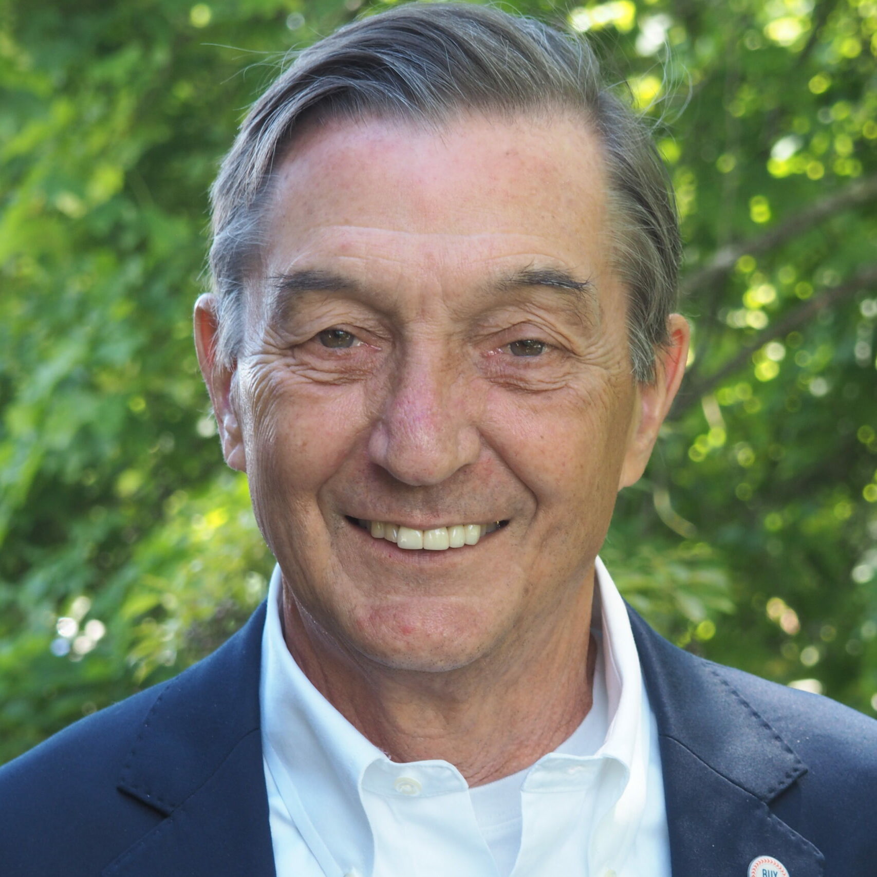 headshot of David Lepage wearing a suit while he smiles in front of greenery.