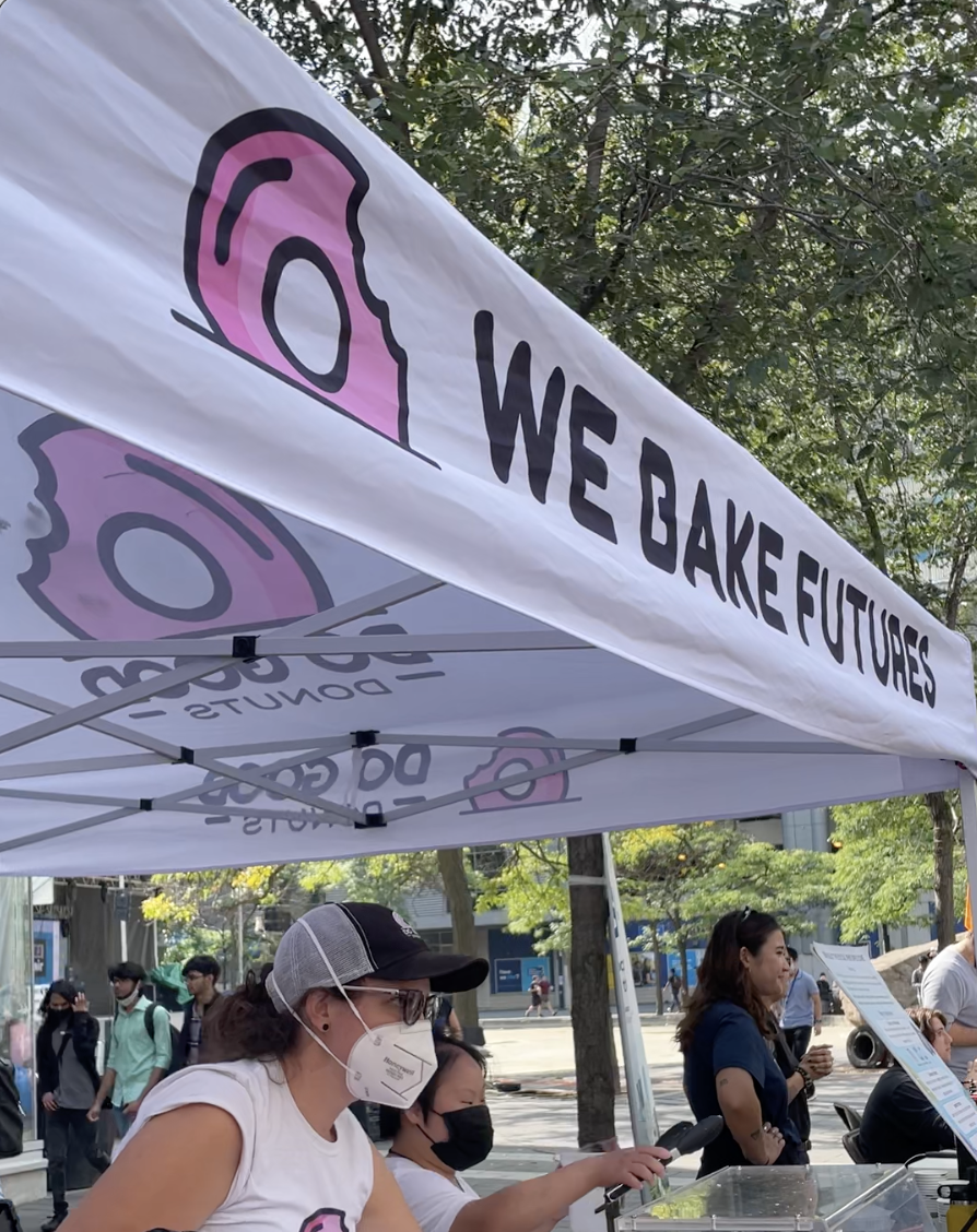 A market vendor tent with a donut on it that says "We bake futures"