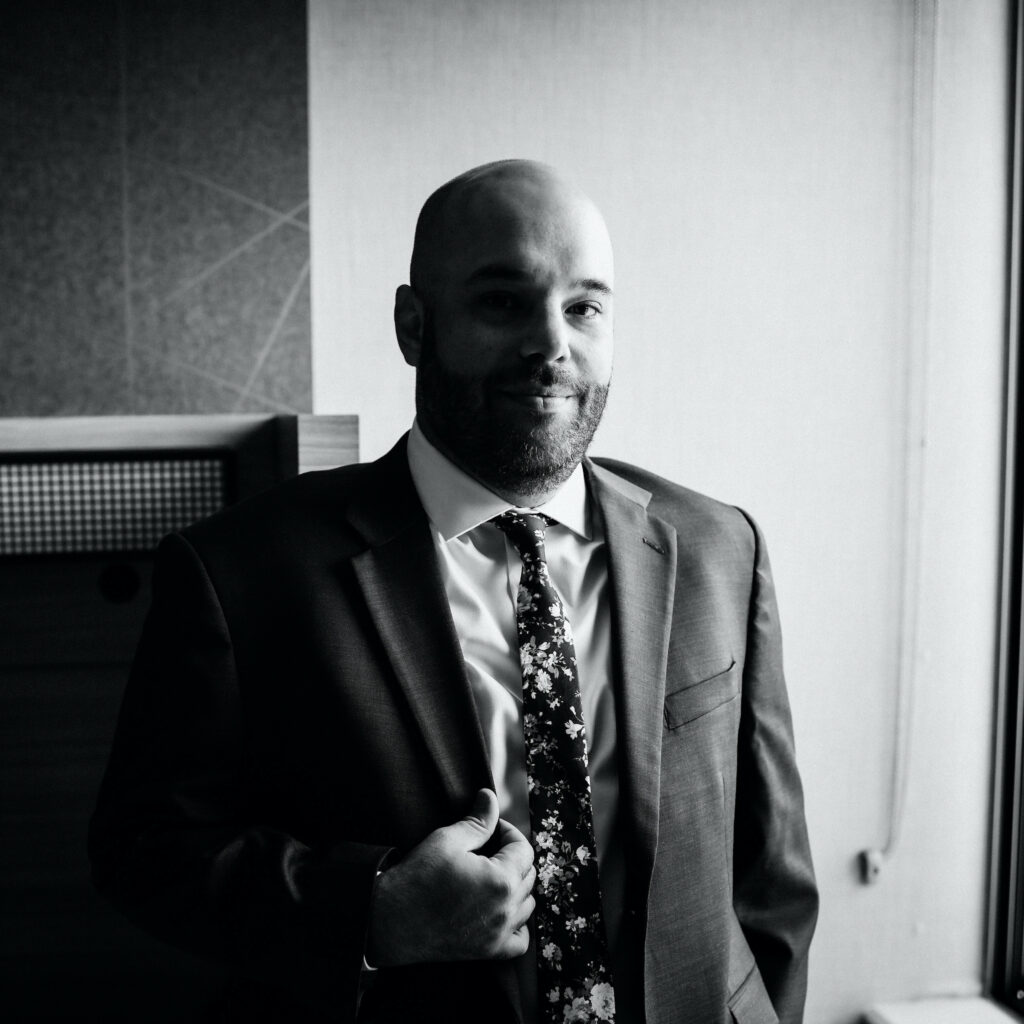 Black and white headshot of Stephen Young standing near a window, wearing a suit.