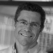 Black and white tight cropped headshot of Martin Loosemore. he wears glasses, a collared shirt, and is smiling.